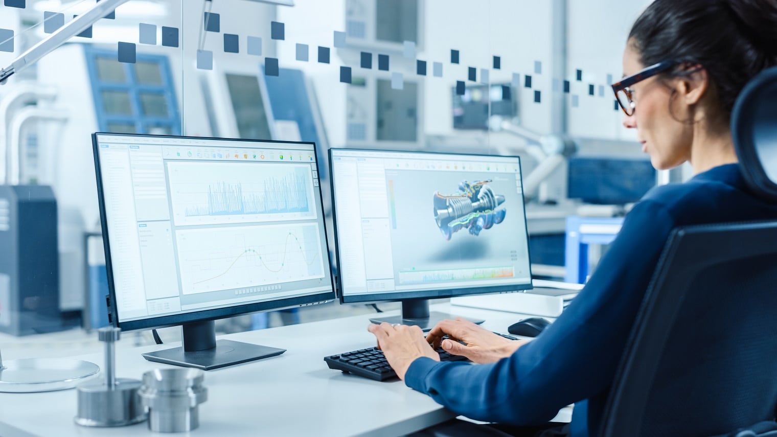 Industrial Female Engineer Working on a Personal Computer, Two Monitor Screens Show CAD Software with 3D Prototype of New Hybrid Hydrogen Engine and Charts. Modern Factory with High-Tech Machinery